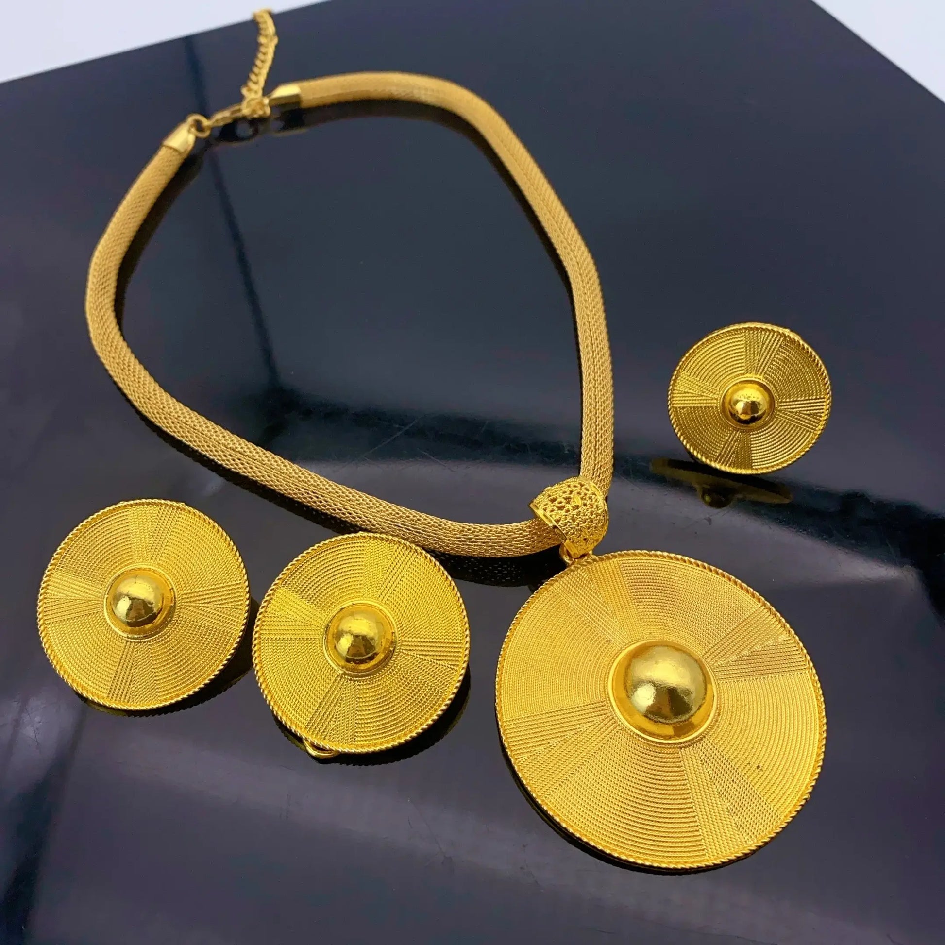 Gold necklace and earrings on a dark surface