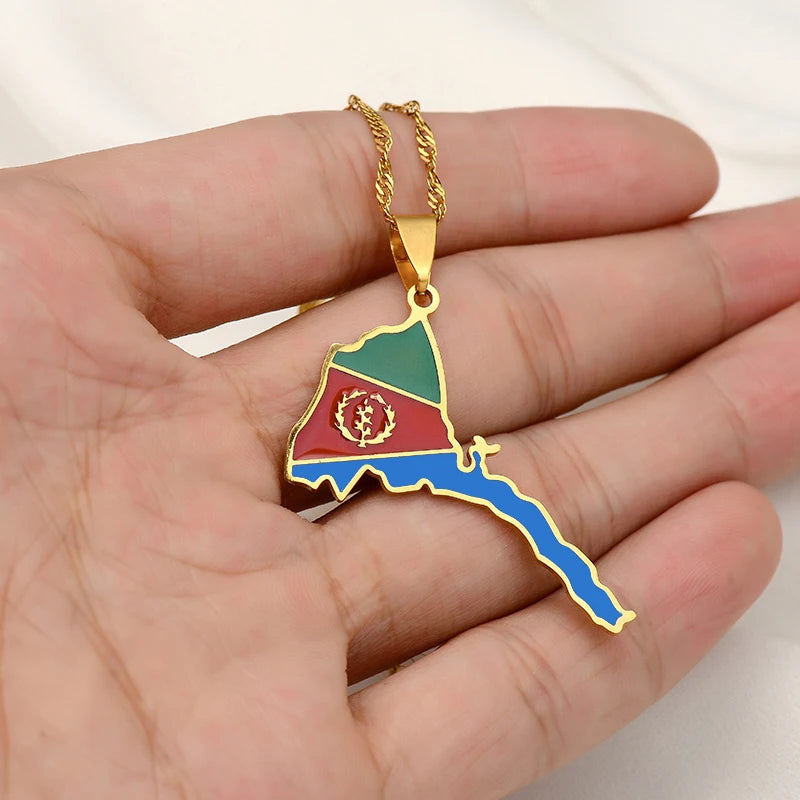 Gold necklace with a pendant shaped like a map, held in a hand against a white background