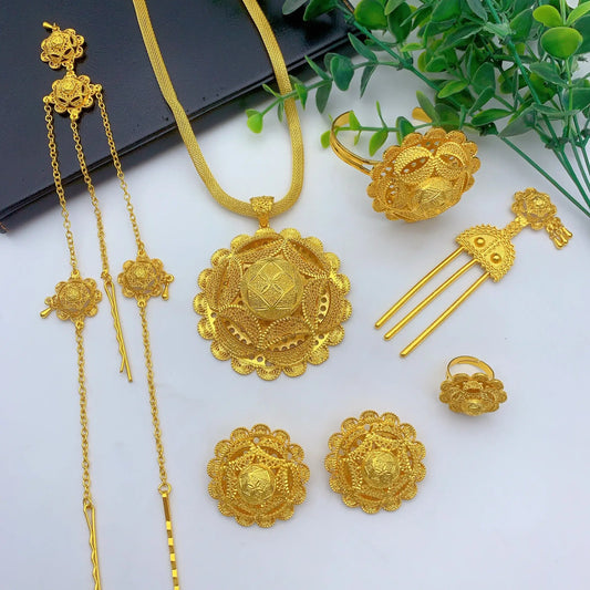 Gold jewelry set including necklace, ring, earrings, and hairpin on a white surface with green leaves.
