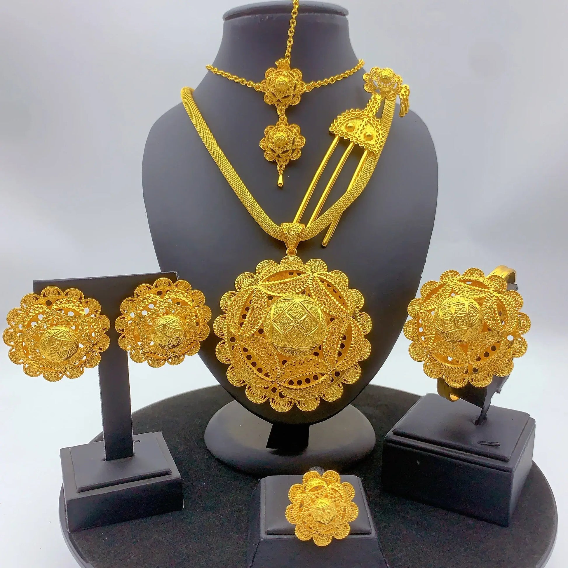 Gold jewelry set including necklace, earrings, and ring on a black stand with a white background