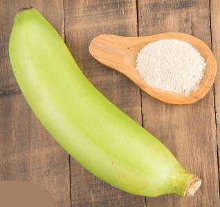 Green banana and wooden spoon with white powder on a wooden surface