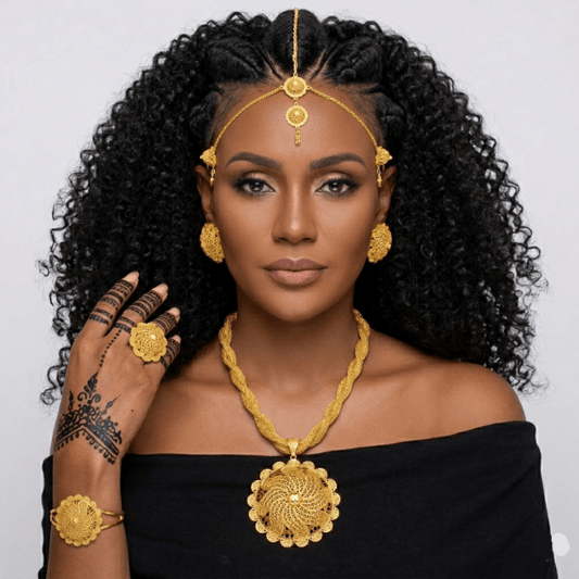Woman wearing gold jewelry including a headpiece, necklace, earrings, and bracelet on a plain background.